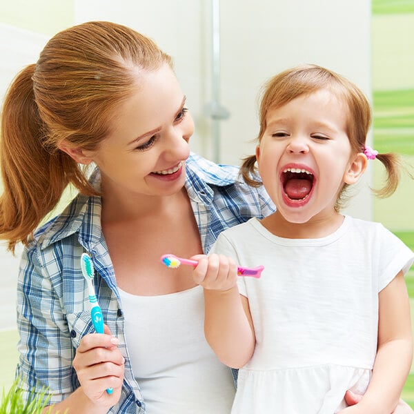 A young mom teaching her little daughter how to brush her teeth before visiting Farm Park Pediatric Dentistry